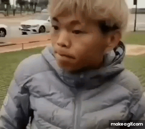 a young boy in a blue jacket is standing in front of a white car and making a funny face .