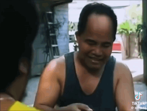 a man in a tank top is smiling and talking to another man in a yellow shirt .