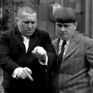 two men in suits and ties are standing next to each other . one of the men is pointing at the camera .