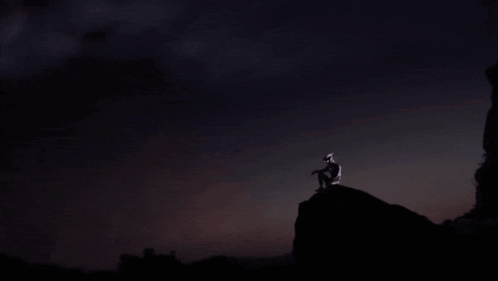 a silhouette of a person standing on top of a mountain with a blue sky in the background