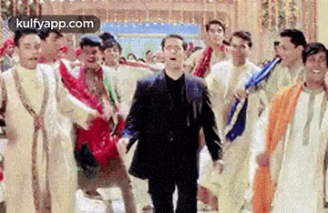 a man in a suit is dancing with a group of men in traditional clothes .
