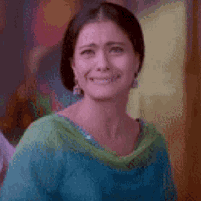 a woman in a blue and green shirt is smiling and making a funny face .